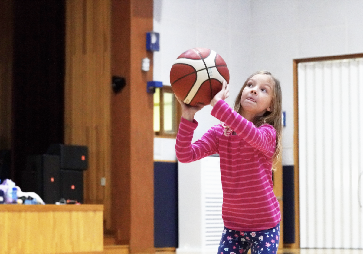 Third-grader Vivienne Vis concentrates intently as she attempts to shoot the basketball into the hoop, her determination drawing cheers from those around her.